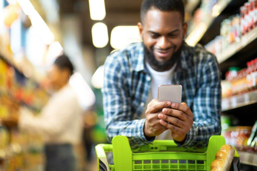 Black Man Using Coupon App For Groceries Shopping In Supermarket