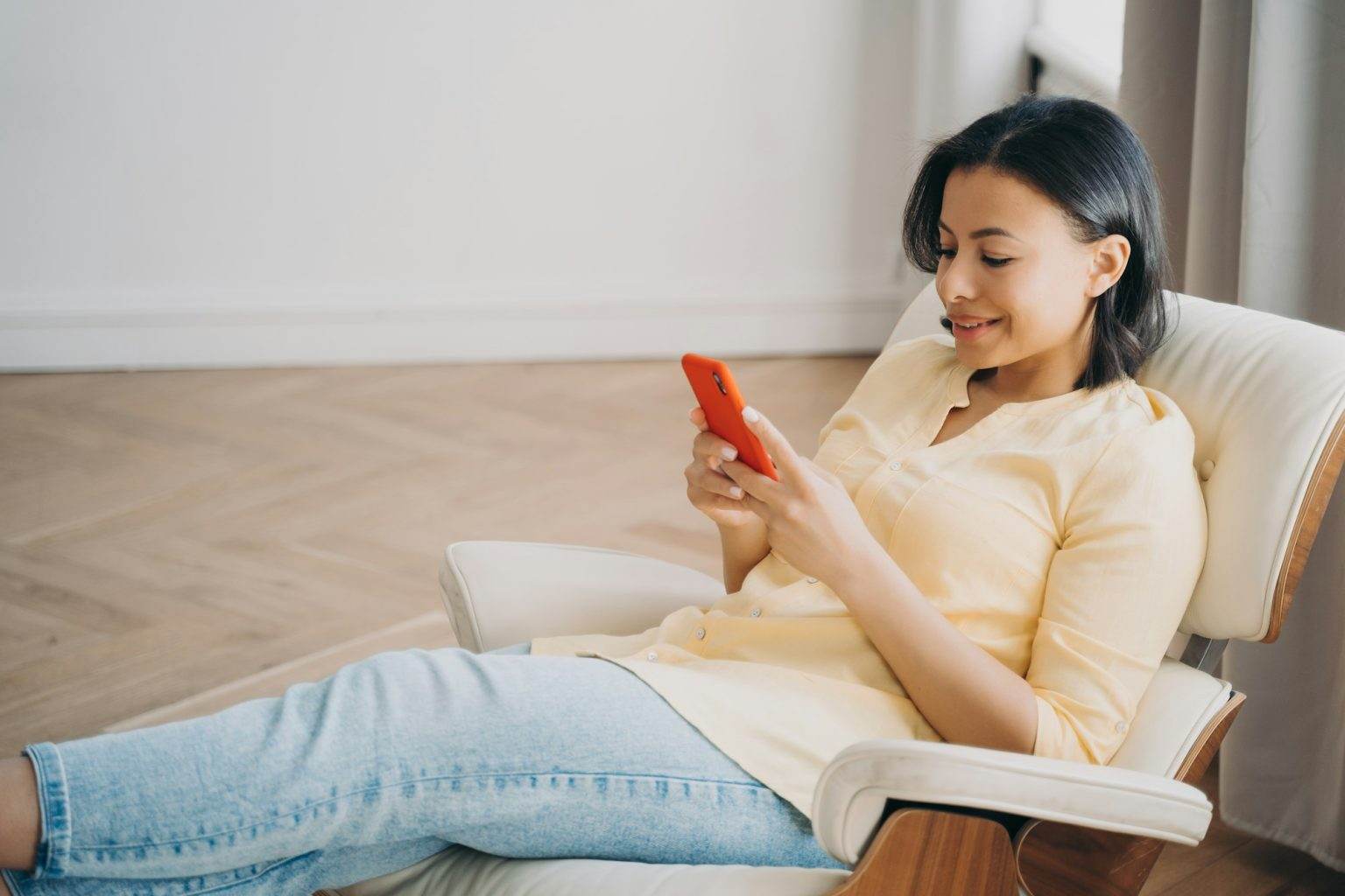 Female using phone sitting in comfortable armchair at home, shopping online. Mobile apps advertising