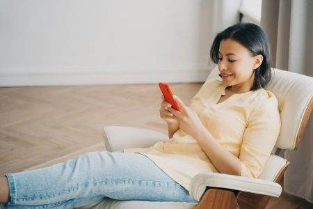 Female using phone sitting in comfortable armchair at home, shopping online. Mobile apps advertising