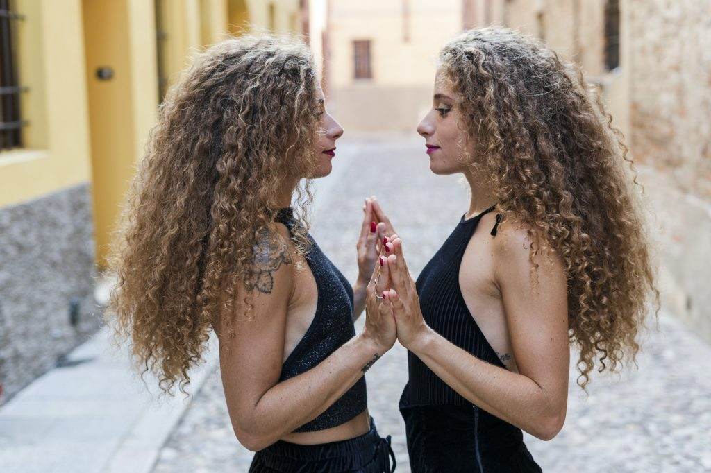 Side view of twin sisters standing face to face touching hands