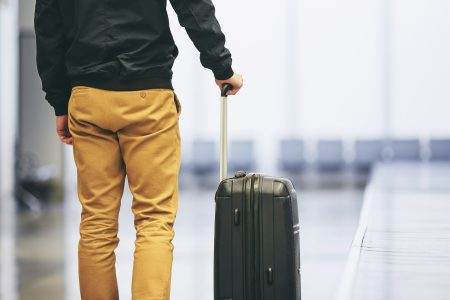 Man traveling by airplane. Young passenger holding his suitcase in airport terminal.