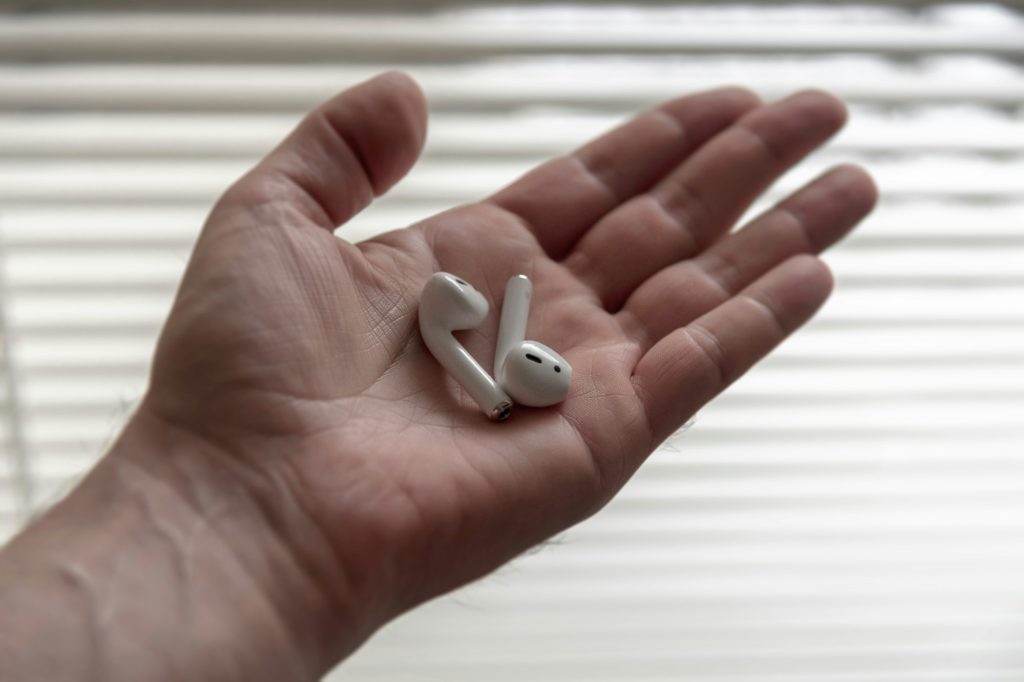 Wireless Apple AirPods headphones in palm of hand close up view next to bright light window shades