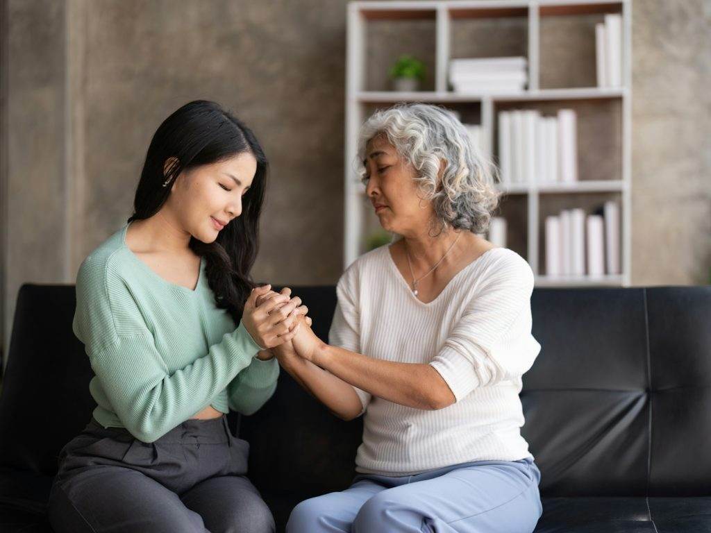 Daughter talking to sad mother holding hand comforting upset having problem