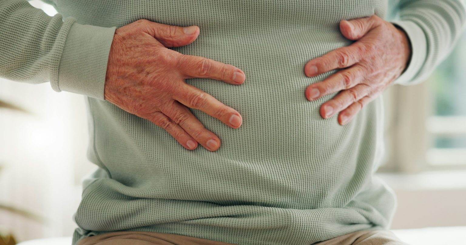 Hands on stomach, closeup and gut health, digestion and nutrition with elderly care and person has