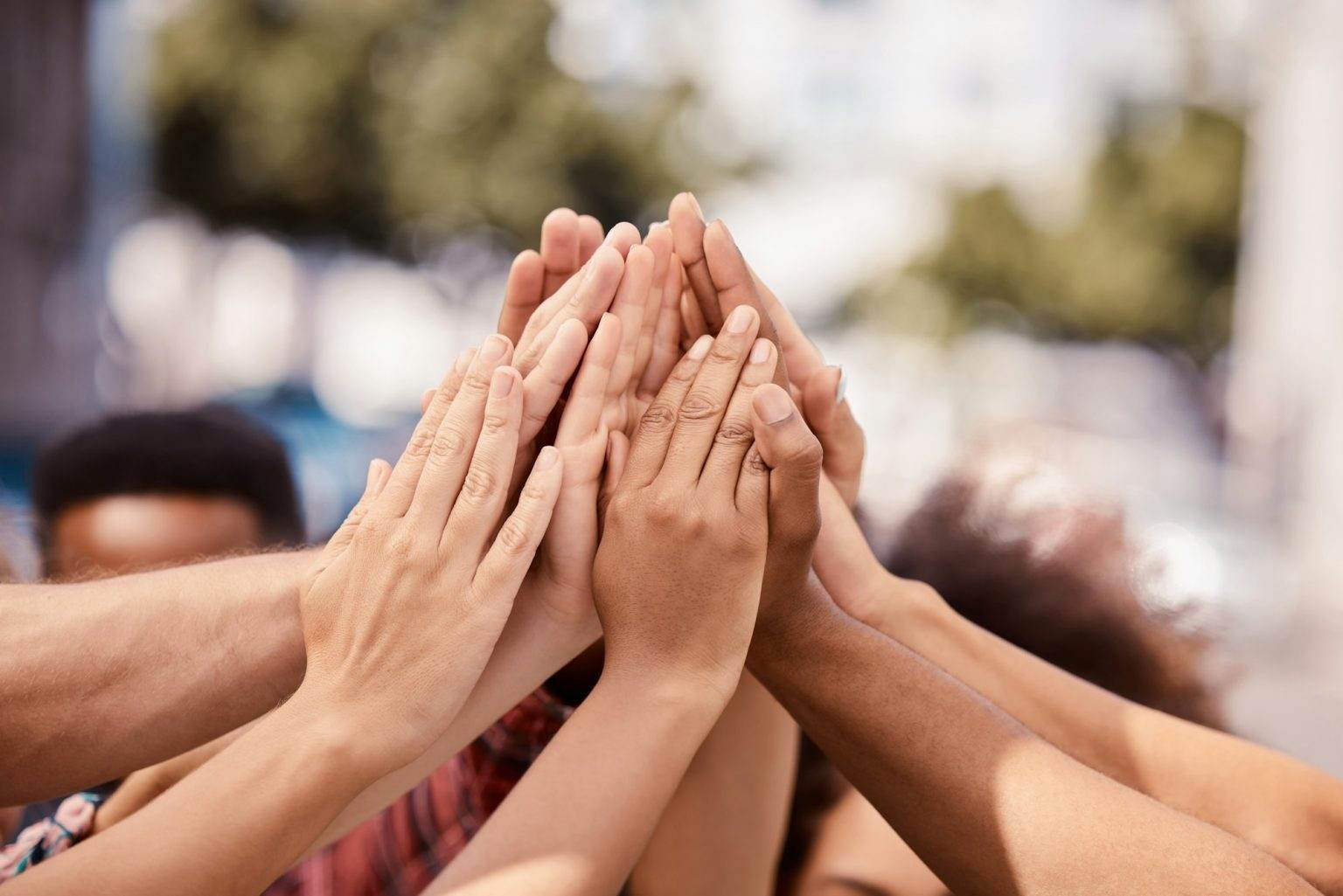 Hands, teamwork and solidarity with a group of people standing outdoor in the city in a huddle or c