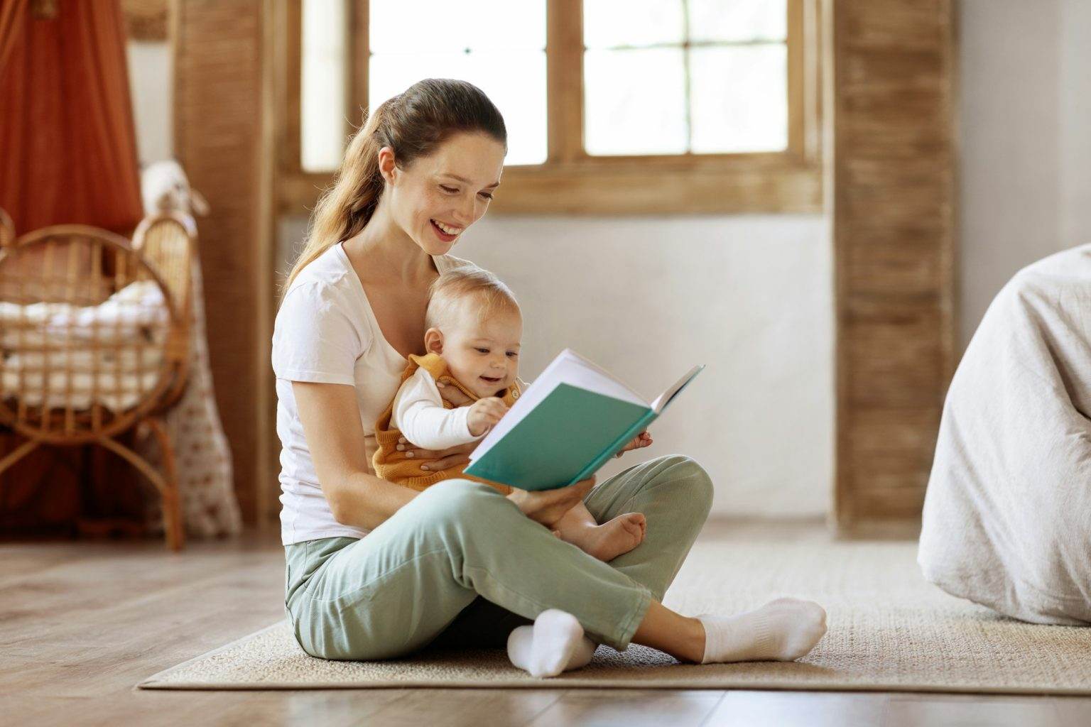 Comment faire un carnet de voyage pour enfant ? Smiling young mother read book with small baby at home