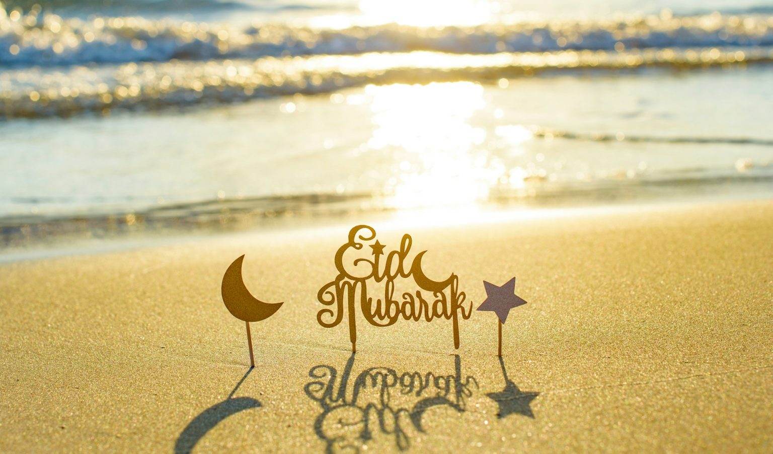 text Eid Mubarak (in English Happy Holidays) on the sand by the sea