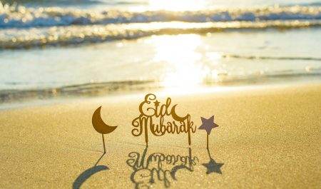 text Eid Mubarak (in English Happy Holidays) on the sand by the sea