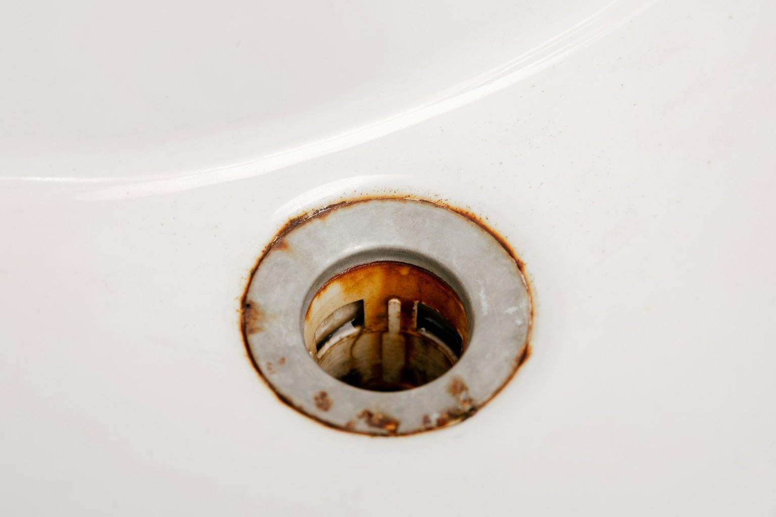 Dirty and rusty washbasin, close up view. Metal drain hole with red rust stain