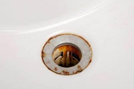 Dirty and rusty washbasin, close up view. Metal drain hole with red rust stain