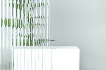 Empty white podium on gray background with plexiglass and ruscus branch behind it. Pedestal podium