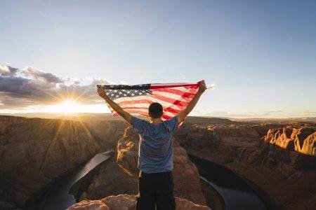 USA, Arizona, Colorado River, Horseshoe Bend, young man on viewpoint with American flag