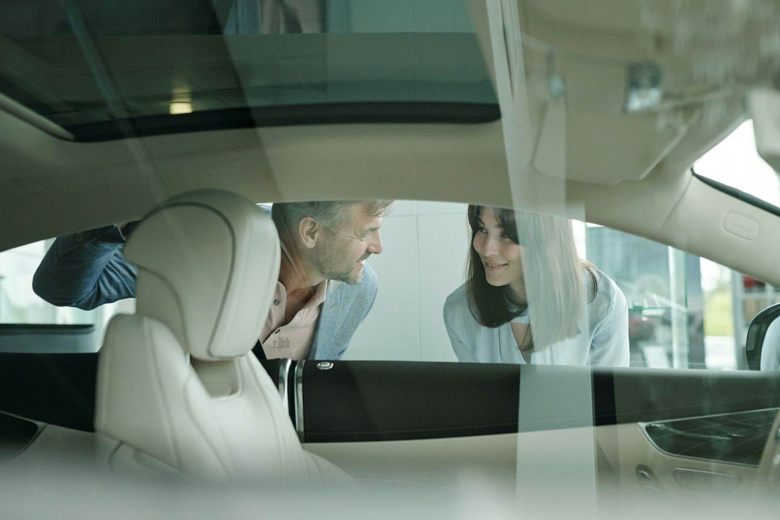 Happy customers standing by car in auto center and bending forwards to window