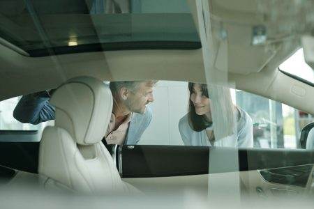 Happy customers standing by car in auto center and bending forwards to window