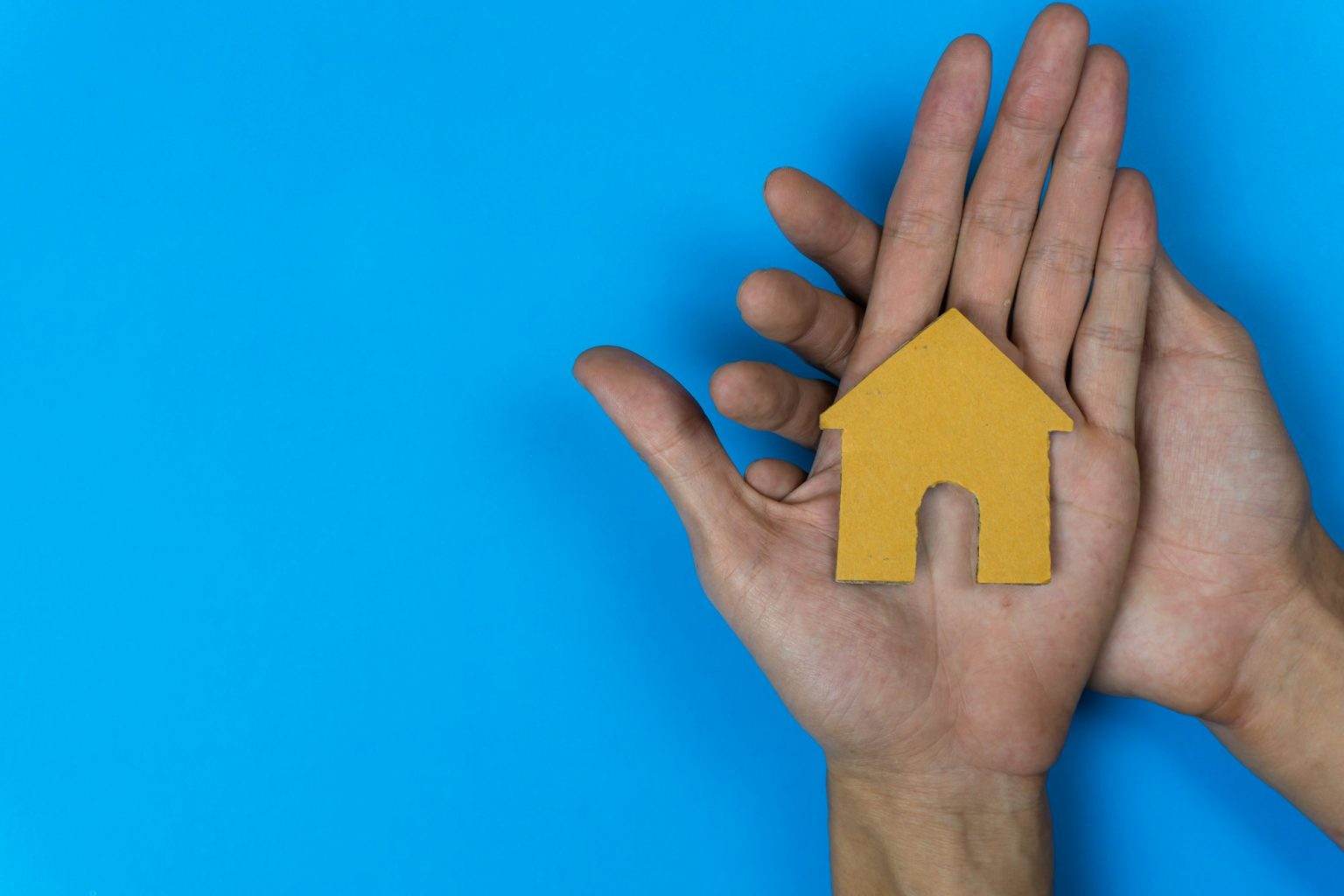 Baisse des frais d’agence pour les locataires – loi Alur Buy or rent. A small house model made by paper cut on a man hand on blue background.