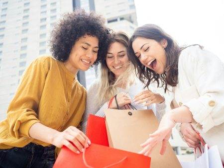 Three smiling multiethnic female friends showing purchases .