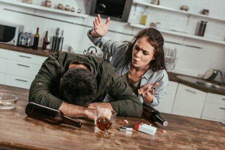 Angry woman quarreling with drunk husband with alcohol addiction on kitchen