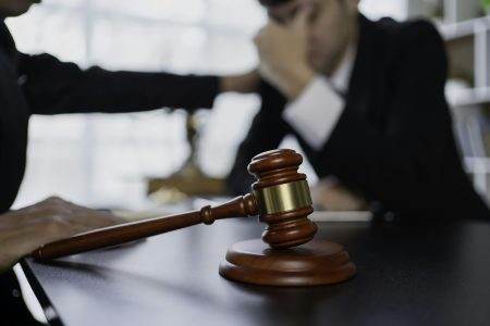 Close-up of a gavel with two people discussing legal matters in a courtroom or office
