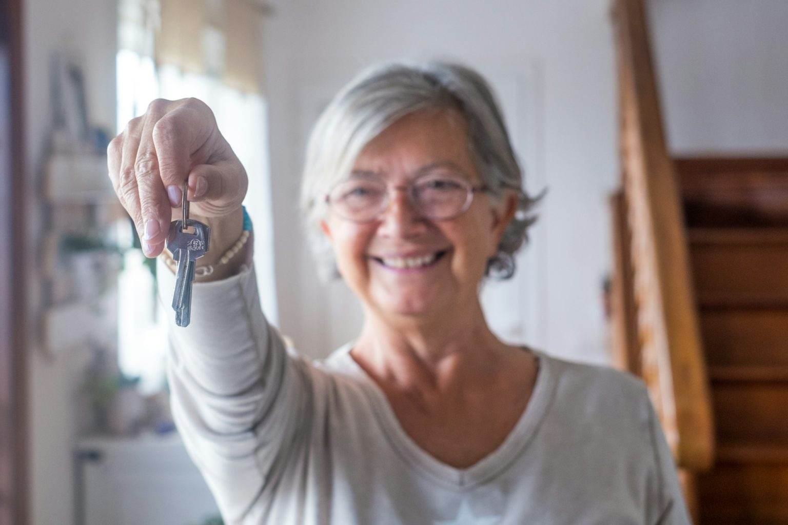 Comment obtenir une aide de la CARSAT pour bien vieillir chez soi ? Close up of old and mature woman at home holding keys of house to the camera.