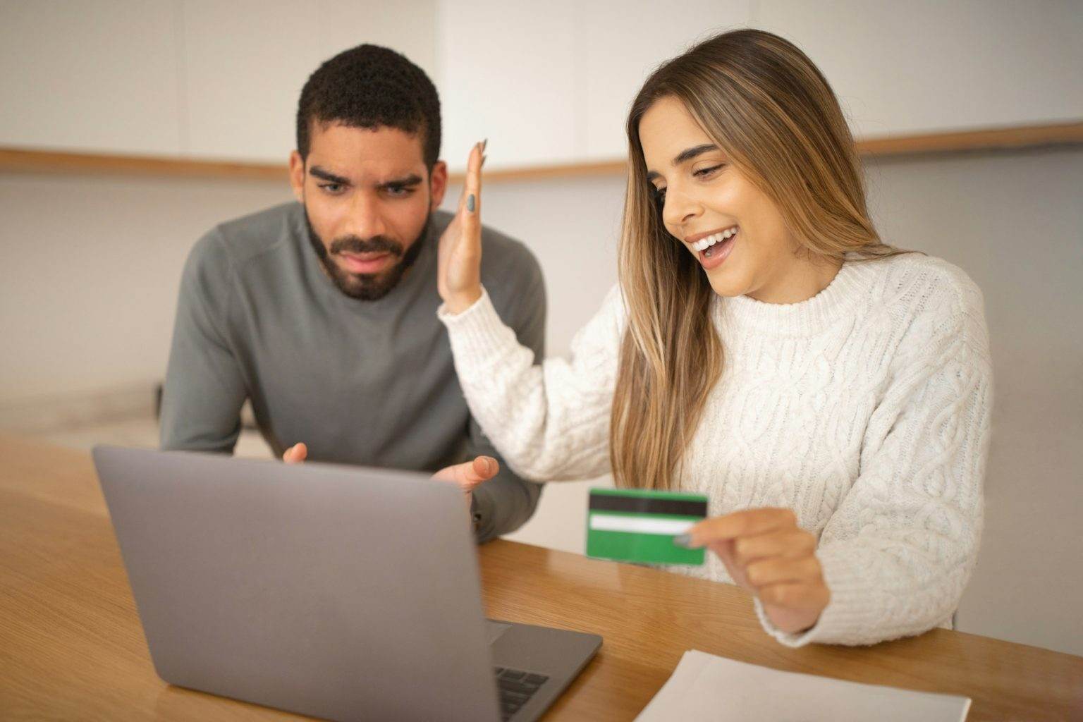 Serious young arab man and laughing european wife with credit card look at computer, lady makes stop