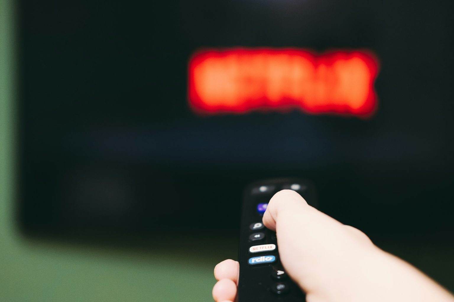 Woman using remote control to switch streaming service on television