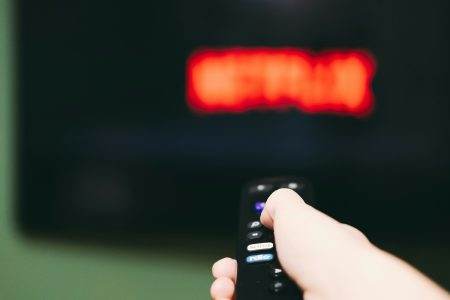Woman using remote control to switch streaming service on television