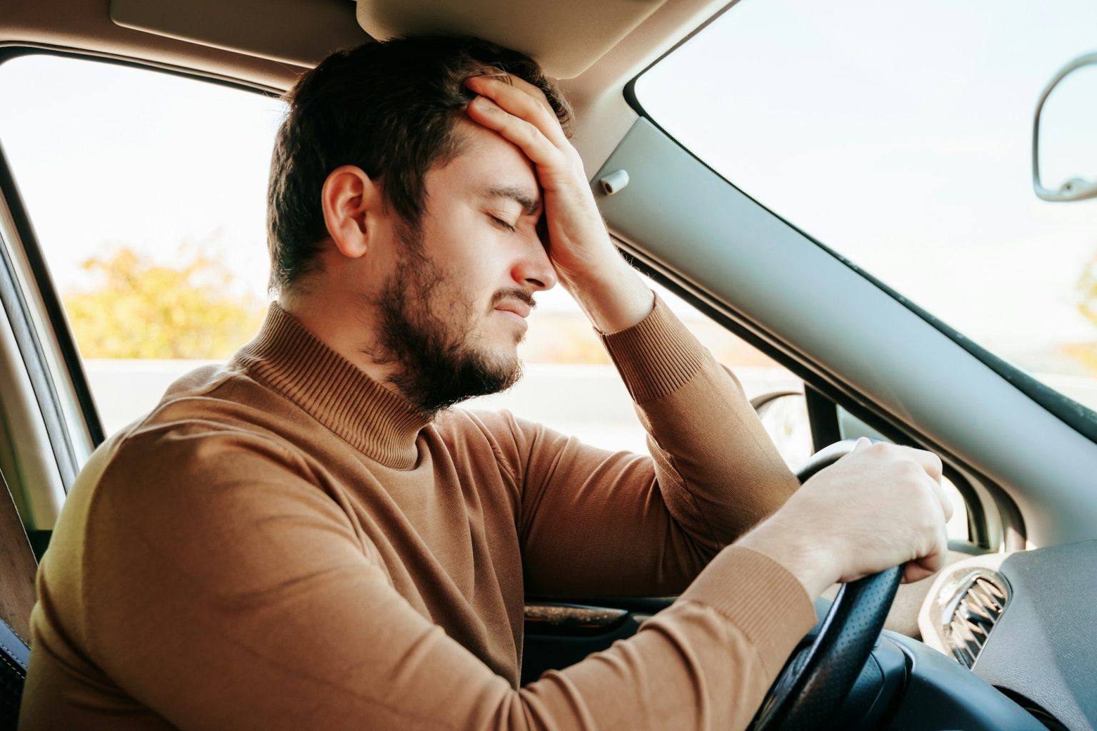 A young guy driver with his eyes closed sits in his car and rests.