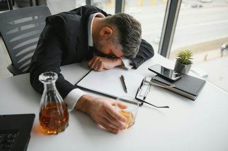 Old business man is drinking alchool at the office