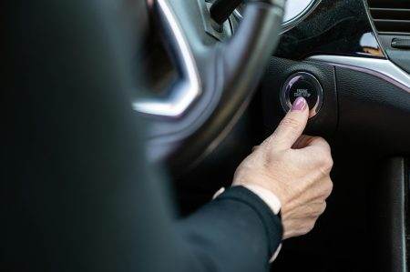 Woman hand pushing on car engine start-stop button. Modern car interior, closeup