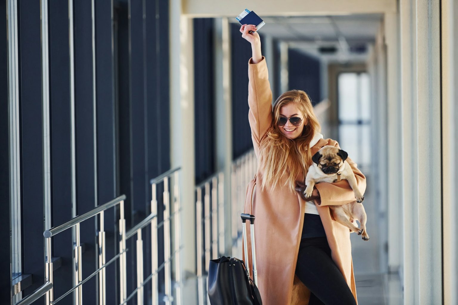 Young female passenger in warm clothes walking with her dog in airport hall