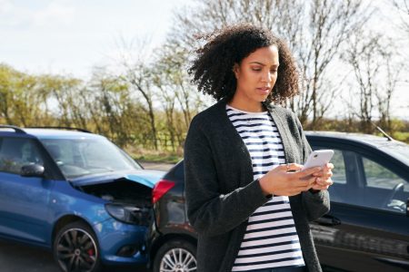 Female Driver Contacting Car Insurance Company On Mobile Phone After Road Traffic Accident