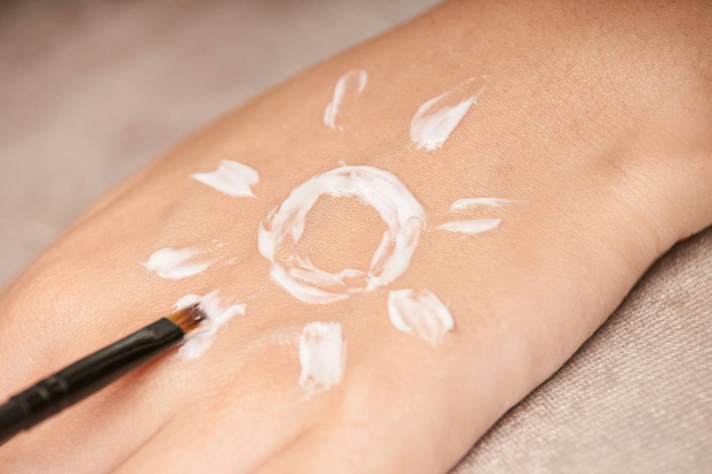 Hand with sun-shaped sunscreen application on skin using brush for skincare