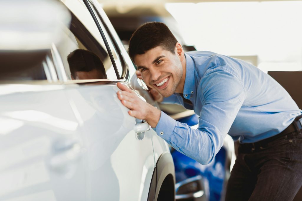 Happy Guy Touching His Auto In Dealership Showroom