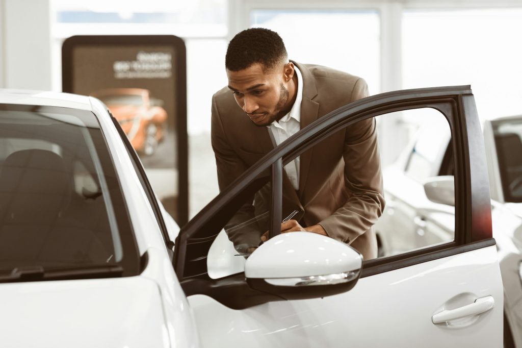 Insurance Agent Checking New Car In Dealership Showroom