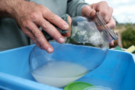 Male hands wash dirty glass jar with sponge in plastic basin in village courtyard