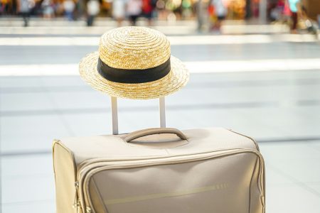 Straw hat on big suitcase, bag in airport terminal. Waiting for boarding to flight. Family