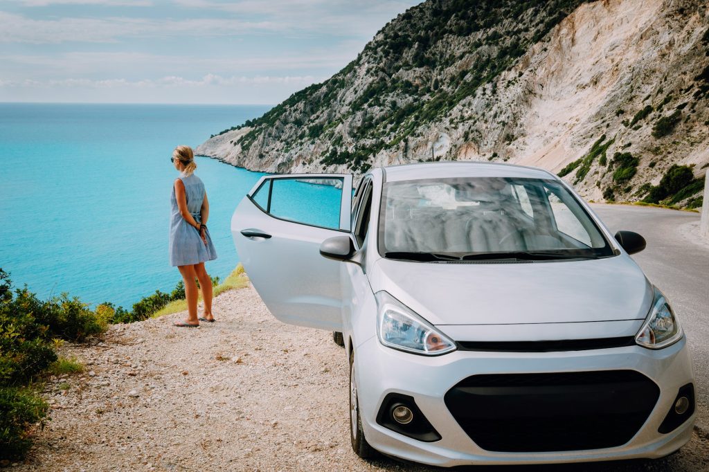 Women near rented car with open door enjoying Myrtos Beach. Travel vocation concept. Kefalonia