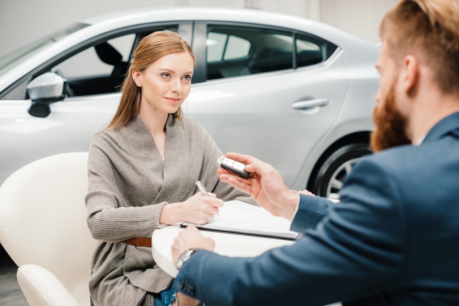Bearded salesman giving new car key to young woman signing papers