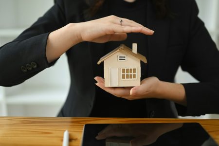 Businesswoman or realtor hands holding a small house model. Real estate and home insurance concept