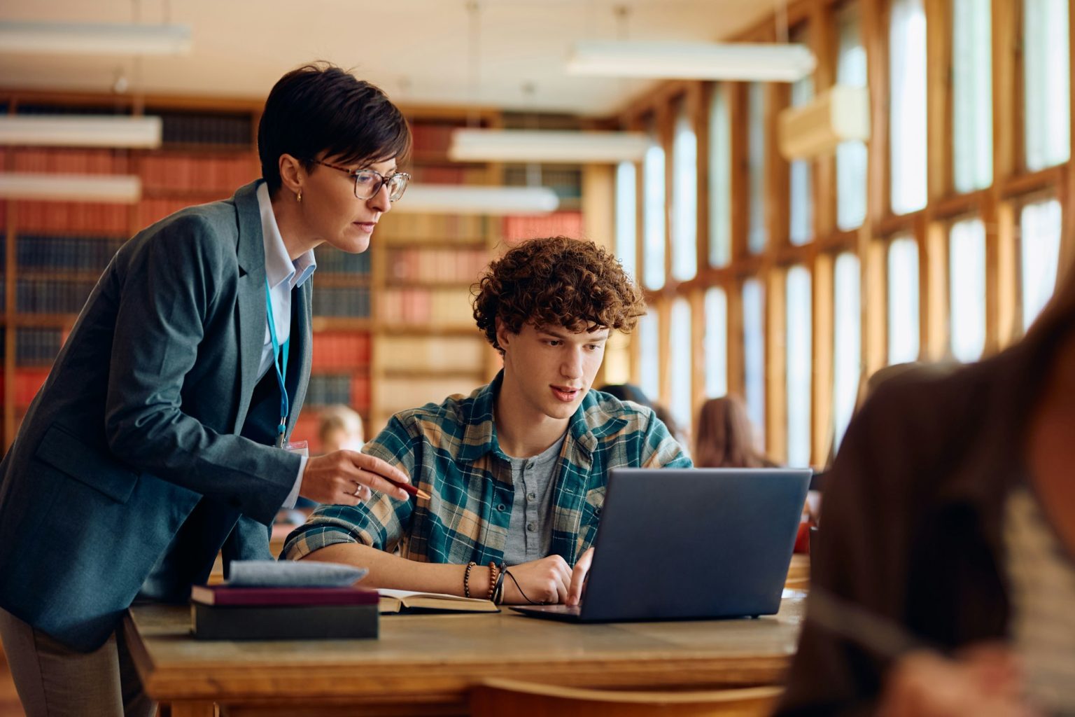 Female professor assisting her student in learning on laptop in the classroom at high school.