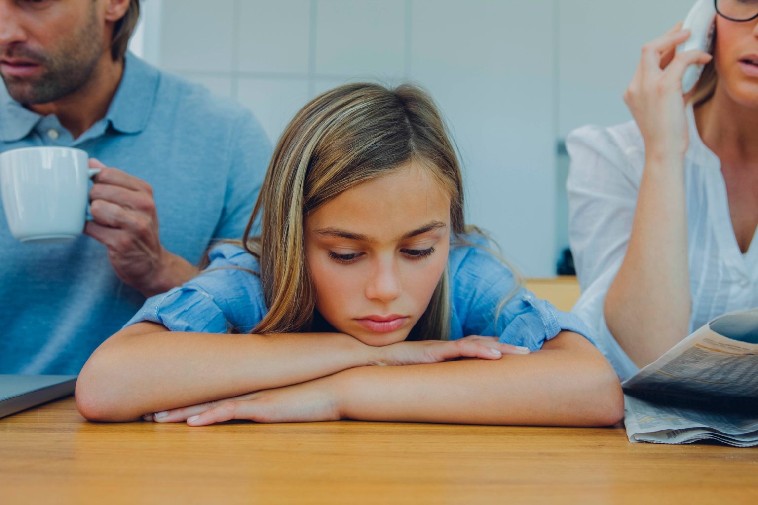 Frustrated girl with distracted parents at table