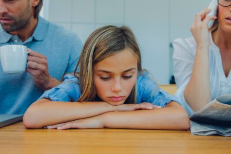 Frustrated girl with distracted parents at table