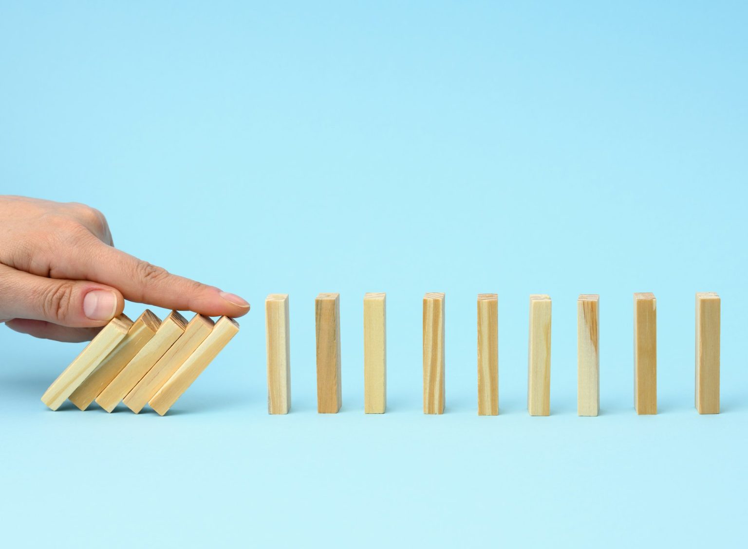 Hand with a finger stops the fall of wooden bars on a blue background