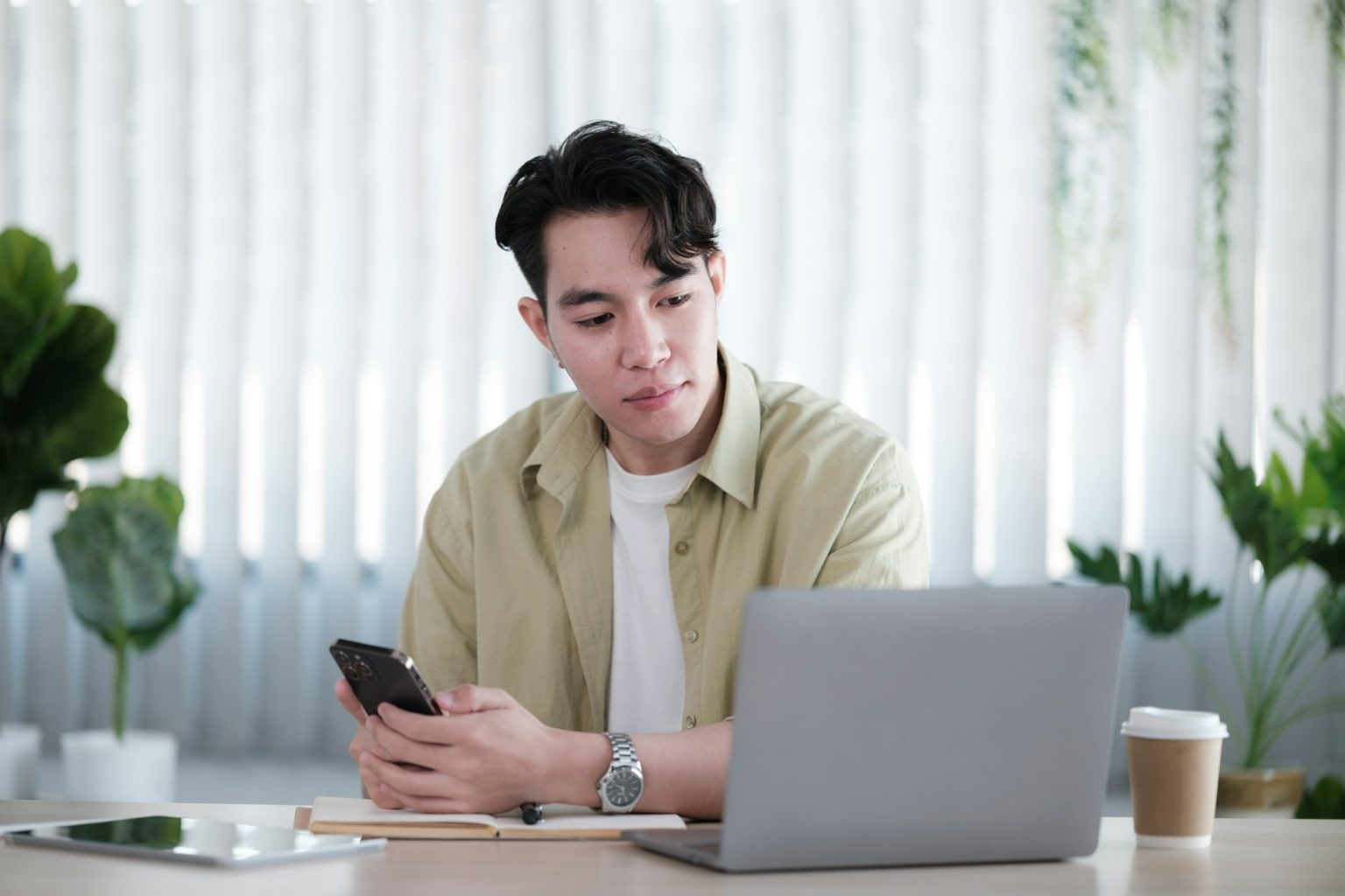 Young man reading sms message from friend on smartphone sitting with laptop device in co working spa