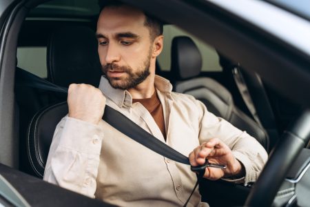 Attractive bearded man holding seat belt, sitting in new car. Transportation, insurance concept