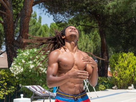 Black boy shakes wet dreadlocks to dry by the pool.