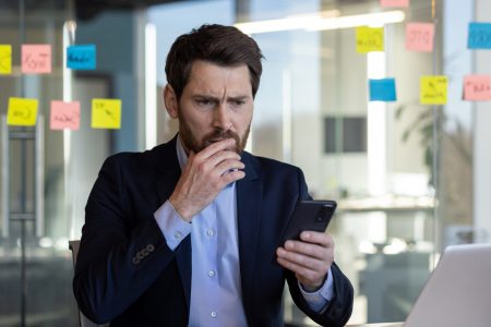 Businessman in office looking concerned at smartphone