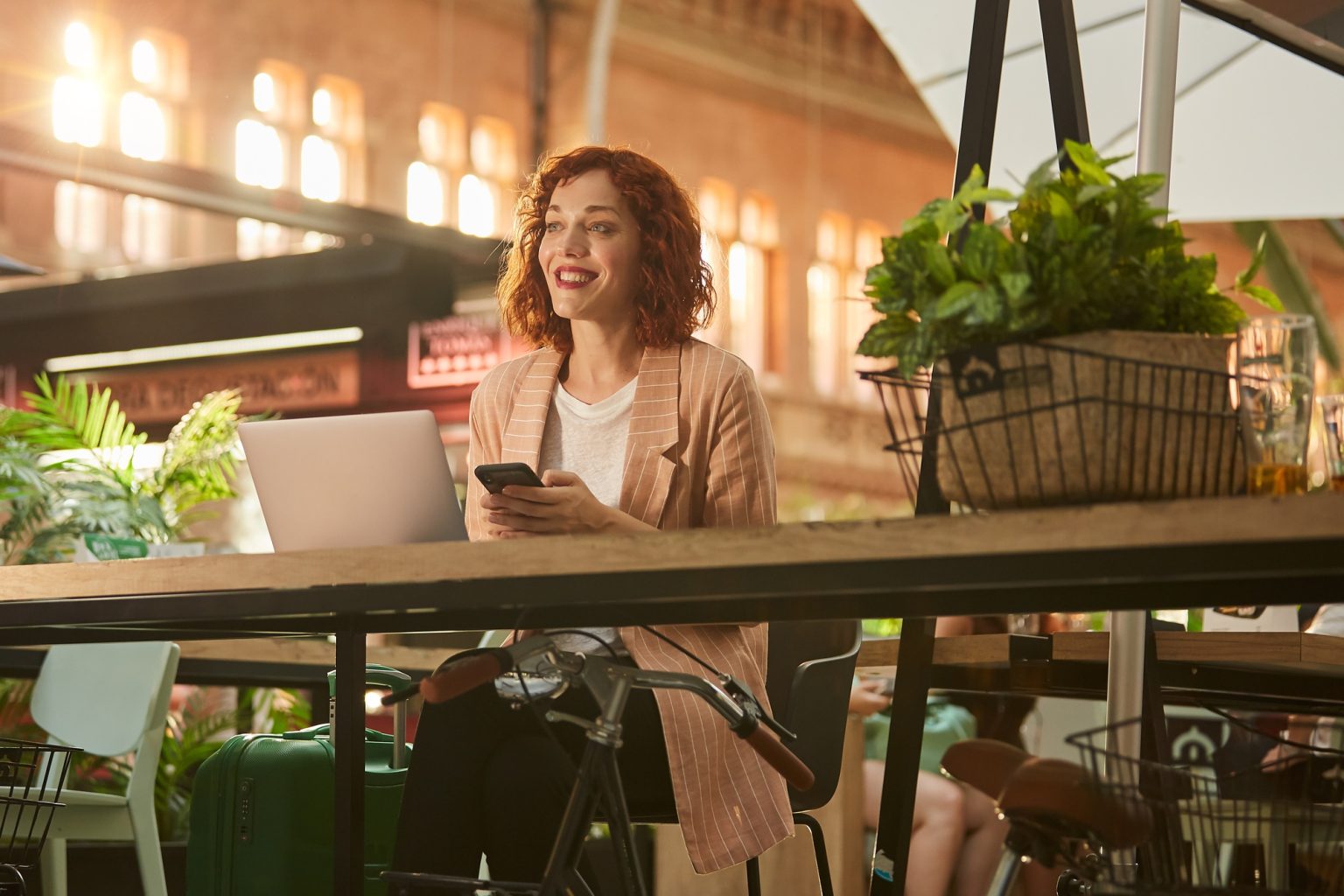 Cheerful young woman working on laptop in cafe and browsing phone