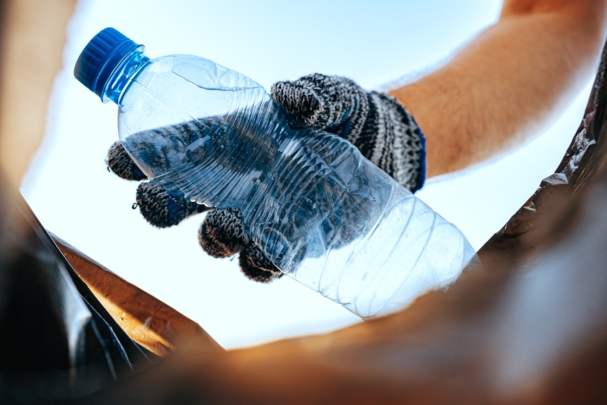 Hand of a man volunteer grabbing plastic litter into a waste bag cleaning up the beach