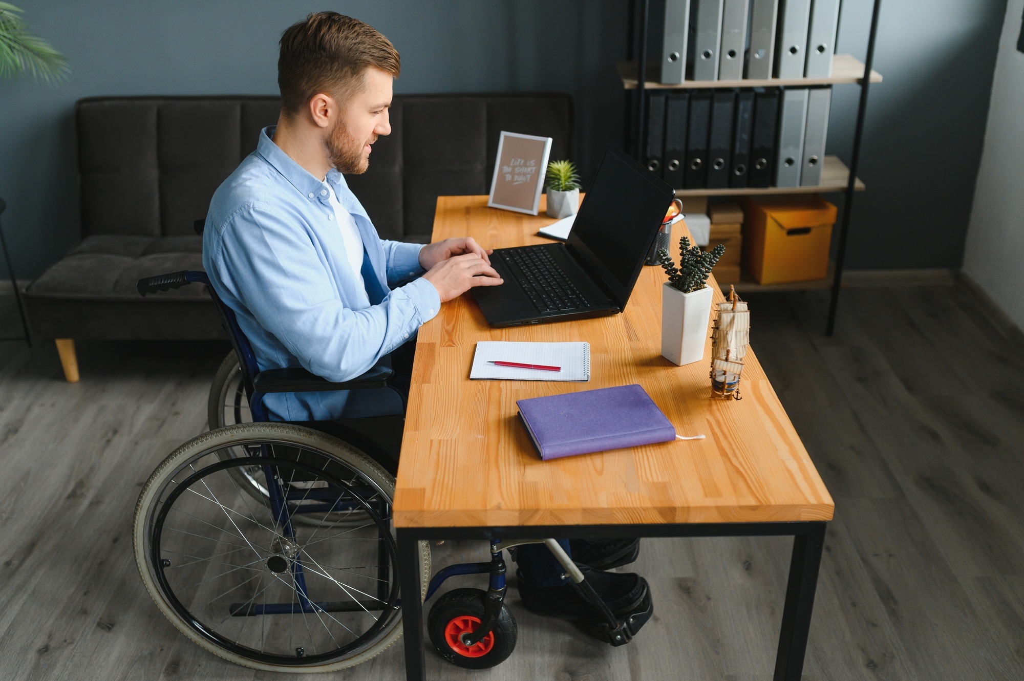 Handicapped Businessman Sitting On Wheelchair And Using Computer In Office